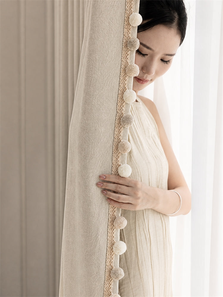 Ivory Maupassant reversible chenille jacquard curtain with pom-pom trim beside a window